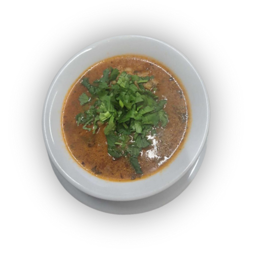 Balta keraminė sriubos lėkštė ant lėkštutės su rudu sultiniu ir žaliu lapiniu