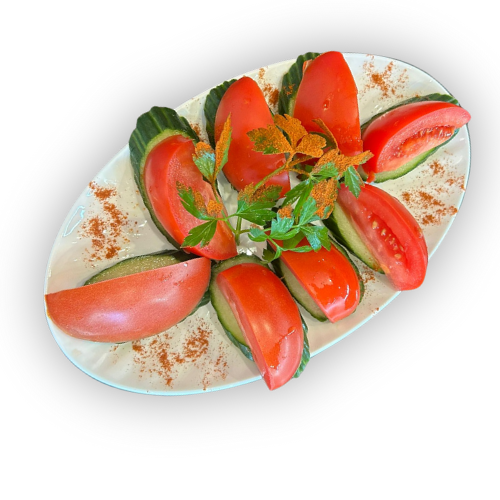 Supjaustyti raudoni pomidorai ir žali agurkai, išdėstyti pakaitomis ant ovalios baltos lėkštės