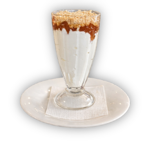 Sluoksniuotas desertas skaidrioje briaunuotoje stiklinėje su baltu kremu, rudu padažo sluoksniu ir